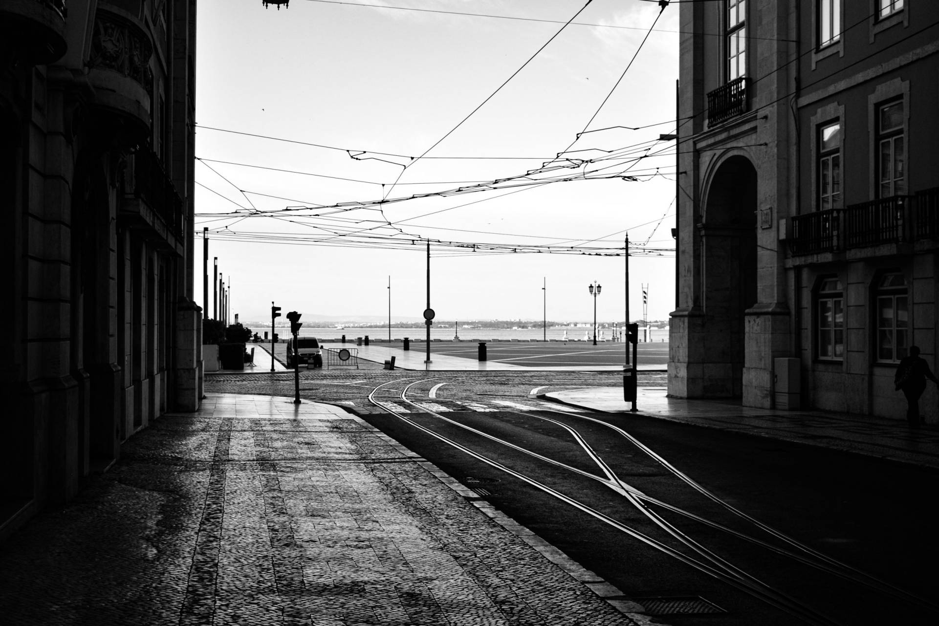 Black and white picture of Praça do Comércio in Lisbon, Portugal taken from an inner street  with trolley lines overhead